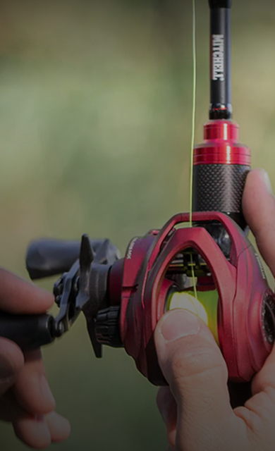 Close-up of a Mitchell Color combo in red with red baitcasting fishing reel spooled with yellow line against a blurred natural background