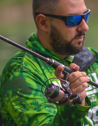 Man in sunglasses, wearing a mixed green coloured jacket, about to cast a fishing rod with spinning reel 