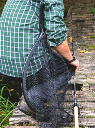 Person holding with a back slung fishing net, holding a fishing rod, crouched on a wooden fishing platform